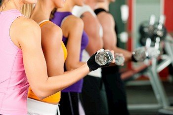 People in gym or fitness club exercising with dumbbells together