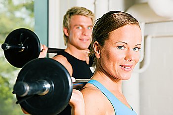 Very attractive and sportive couple doing power gymnastics with barbells