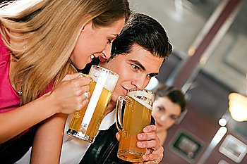 Group of people in a bar or restaurant drinking beer, one couple flirting very obviously having a lot of fun