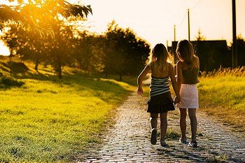 Two sister children on a path leading to the next village, dreamy evening mood in a backlit setting