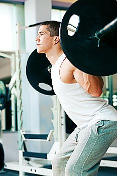 Strong and handsome man lifting weights - a barbell - in a gym