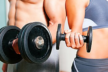 Couple exercising with dumbbells in a gym, focus on eyes of man and woman