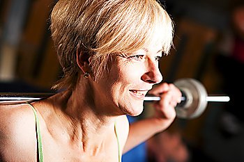Mature woman in a gym exercising by lifting a barbell