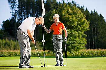 Mature or senior couple playing golf, he is putting at the green