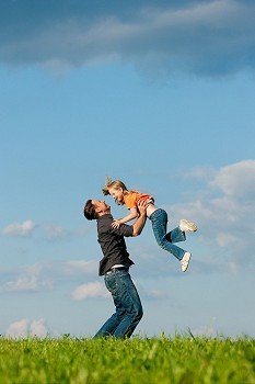 Father and his kid - daughter - playing together at a meadow, he is throwing her into the air at a late summer afternoon, family concept