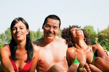Group of friends - man and to women sitting in the sun in summer and having fun enjoying themselves