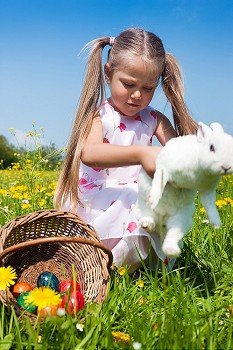 Little girl petting the Easter bunny on a meadow in spring