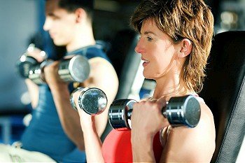 Couple (male / female) exercising with dumbbells in a gym; focus on face of the woman