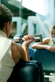 Woman lifting dumbbells in a gym, seeing herself in a mirror (focus only on the dumbbell)