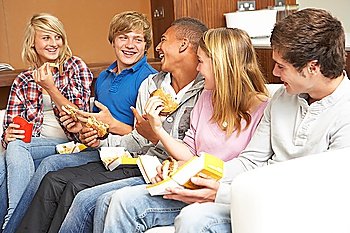 Group Of Teenage Friends Sitting On Sofa At Home Eating Fast Food