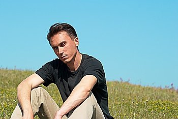 Young man sitting on the grass field with blue sky