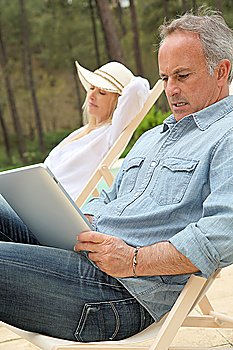 Couple resting in long chairs with electronic tablet