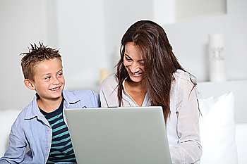 Little boy and mother sitting on sofa at home with laptop
