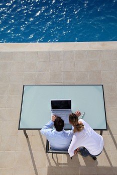 View from above of couple using computer by swimming-pool