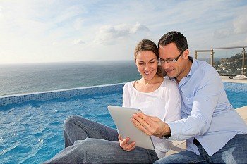 Happy couple using electronic tablet by swimming-pool
