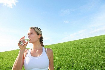 Woman drinking natural water in green field