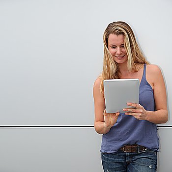 Smiling blond woman using electronic tablet on grey background