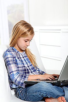 Little blond girl sitting in sofa with laptop computer