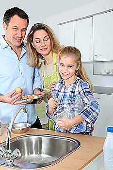 Parents and daughter preparing meal in home kitchen
