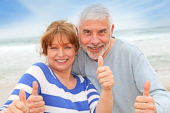 Happy senior couple with thumbs up at the beach