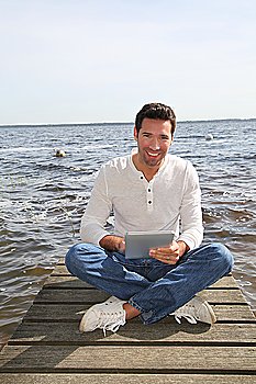 Handsome man sitting on a pontoon with touchpad