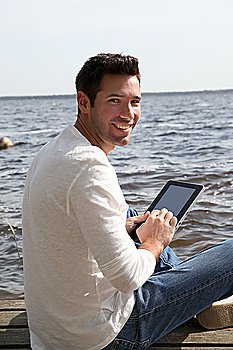 Handsome man sitting on a pontoon with touchpad