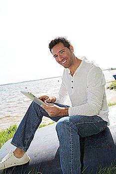 Man sitting on a lakeside with electronic tablet