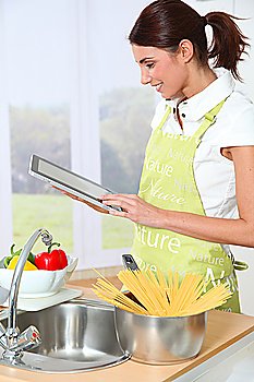 Woman in kitchen looking at recipe on electronic tab