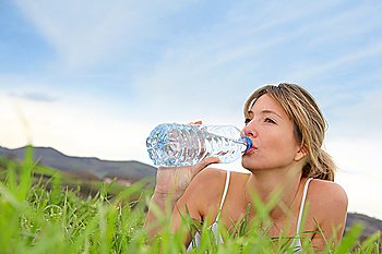 Beautiful blond woman drinking water in natural landscape