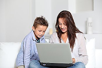 Little boy and mother sitting on sofa at home with laptop