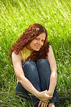 The beautiful young girl sits on a background of a green lawn and smiles
