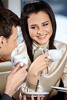 Man and woman in cafe drink coffee and smile, looking against each other