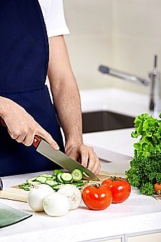 The man in an apron cuts cucumbers close up