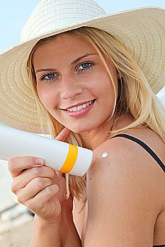 Blond woman putting sunscreen on her shoulder