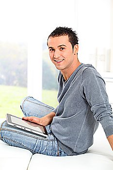 Young man sitting on sofa with electronic pad