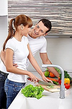 The young girl with the young man cuts vegetables on kitchen