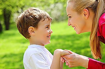 Mother and son look against each other having joined hands in park in spring