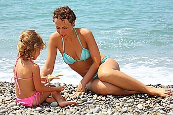 young woman with little girl played starfish on stony beach
