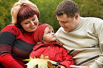 Married couple and little girl sit on a bench in park in autumn