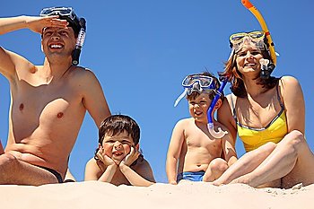 Parents with children in underwater masks sit on sand