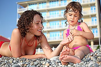 Mother with daughter on pebble in swimwear