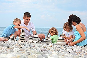 family with three children builds  stone stacks on pebble beach