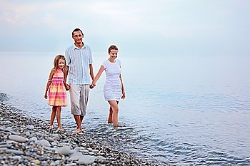 Happy family with little girl walk on beach in evening, focus on mother