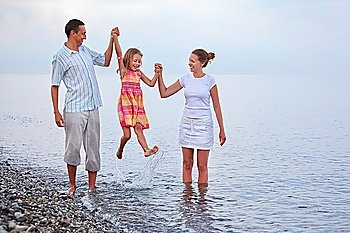Happy family with little girl on beach in evening, parents lift girl for hands
