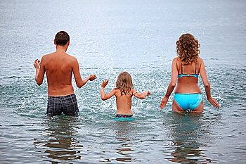 Happy family with little girl splashes water hands standing on belt in sea, standing back