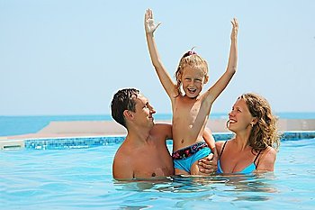 smiling parents play with daughter with hands up in water
