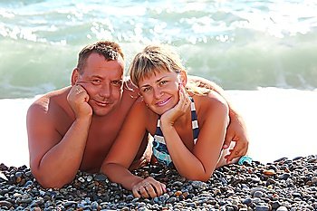 middleaged pair lie on pebble beach