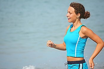 smiling woman wearing sporty clothers is running near water. sea in out of focus.