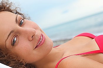 beautiful woman wearing swimsuit is laying near water on sea coast