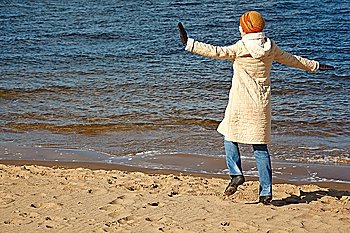 Cheerful girl walks on beach in solar autumn day. In coat, cap and jeans.